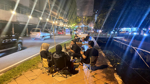 Pengunjung tampak bersantai menikmati kopi di pinggir jalan pada malam hari. Foto: Alycia Tracy Nabila/Hi!Pontianak