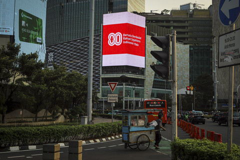 Seorang pedagang melihat Videotron yang menampilkan logo HUT RI ke-80 di kawasan Jalan Sudirman, Jakarta, Kamis (24/7/2025). Foto: Iqbal Firdaus/kumparan