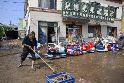 Seorang pria membersihkan sisa-sisa banjir usai hujan lebat di distrik Miyun, pinggiran Beijing, pada Senin (28/7). Foto: Jade Gao/AFP