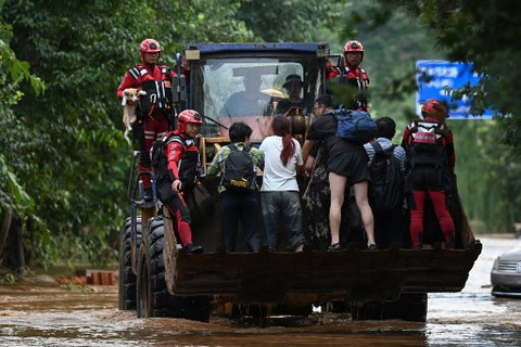 Sejumlah warga menaiki kendaraan berat menghindari area banjir di Miyun, Beijing, pada Senin (28/7). Foto: Jade Gao/AFP