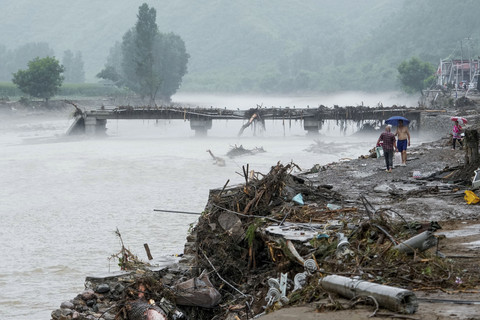 Orang-orang berjalan melewati jembatan yang rusak setelah hujan deras membanjiri area tersebut, di distrik Huairou, Beijing, China, Senin (28/7/2025). Foto: Stringer/REUTERS