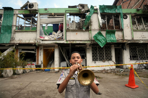 Juan Manuel Tejada, seorang siswa sekolah menengah militer, memainkan terompet di depan sebuah bangunan yang rusak oleh Bom, Cali, Kolombia, Jumat (8/22/2025). Foto: Jair F. Coll/Reuters