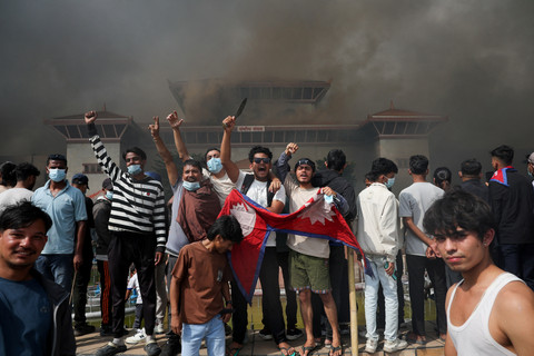 Demonstran memegang bendera Nepal saat asap mengepul di kompleks Parlemen, Kathmandu, Nepal, Selasa (9/9/2025). Foto: Adnan Abidi/REUTERS