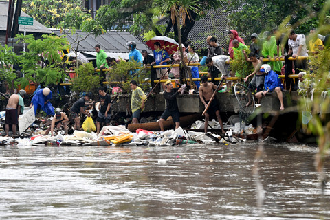 Sejumlah warga membersihkan sampah di area jembatan saat banjir akibat hujan deras di Denpasar, Bali, Rabu (10/9/2025). Foto: Sonny Tumbelaka/AFP