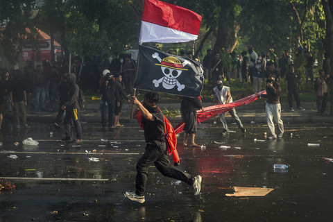 Demonstran membawa bendera one piece saat aksi menuntut pengusutan kasus penabrakan pengemudi ojek daring Affan Kurniawan oleh mobil rantis Brimob di depan kantor Gubernur Surabaya, Jawa Timur, Jumat (29/8/2025). Foto: Juni Kriswanto/AFP