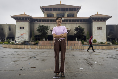 Seorang pelajar, Sunita Khadka (21) berpose dengan latar belakang gedung Parlemen yang terbakar di vandalisme saat mengikuti aksi menentang korupsi di Kathmandu, Nepal. Foto: Navesh Chitrakar/Reuters