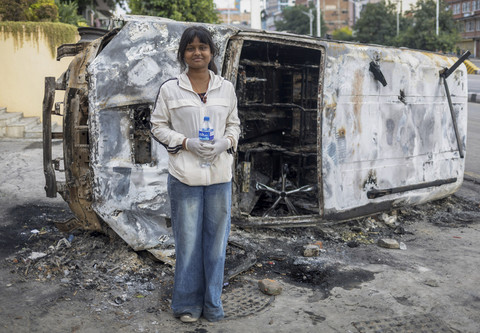 Seorang pelajar, Amrita Tiwari (17) berpose dengan latar belakang mobil yang hangus terbakar saat mengikuti aksi menentang korupsi di Kathmandu, Nepal. Foto: Navesh Chitrakar/Reuters