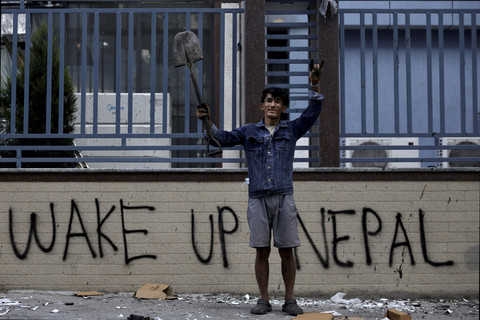 Seorang pekerja restoran, Sabin Tamang (20) memegang sekop dan berpose dengan latar belakang tembok yang di vandalisme saat mengikuti aksi menentang korupsi di Kathmandu, Nepal. Foto: Navesh Chitrakar/Reuters