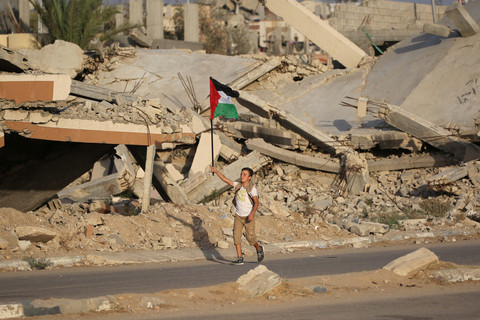 Seorang anak mengibarkan bendera Palestina sambil berjalan melewati reuntuhan bangunan di kamp pengungsi Bureij, Jalur Gaza tengah, Senin (22/9/2025). Foto: Eyad BABA / AFP