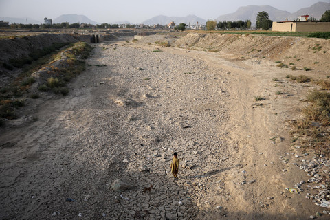 Seorang anak laki-laki mengawasi seekor anjing sambil berdiri di dasar sungai Kabul yang mengering, di tengah krisis air yang parah di Kabul, Afghanistan. Foto: REUTERS/Sayed Hassib