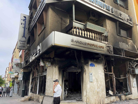 Warga melintas di dekat bangunan yang terbakar yang dulunya merupakan bank usai aksi unjuk rasa yang dipimpin oleh pemuda yang menuntut pendidikan dan layanan kesehatan yang lebih baik di pusat kota Casablanca, Maroko, Kamis (2/10/2025). Foto: Ahmed El Jechtimi/Reuters