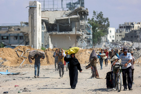 Warga Palestina yang mengungsi berjalan di sepanjang jalan yang rusak parah melewati bangunan-bangunan yang hancur di pusat Khan Yunis di Jalur Gaza selatan, Jumat (10/10/2025). Foto: Omar AL-QATTAA / AFP