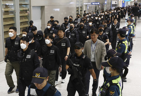 Petugas kepolisian mengawal warga Korea Selatan yang dideportasi dan ditahan oleh otoritas Kamboja atas dugaan keterlibatan dalam operasi penipuan siber setibanya di Bandara Internasional Incheon, Seoul, Korea Selatan, Sabtu (18/10/2025). Foto: Yonhap/AFP