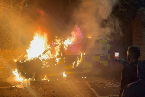 Warga merekam sebuah kendaraan polisi yang terbakar saat demonstrasi di luar sebuah hotel tempat para pencari suaka bergejolak di Saggart, barat daya Dublin, Irlandia, Selasa (21/10/2025). Foto: PETER MURPHY/AFP