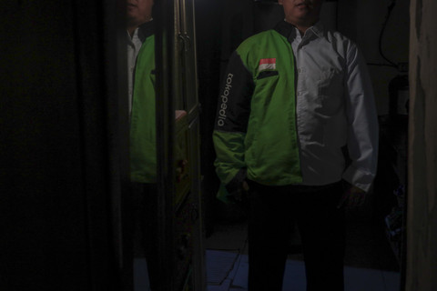 Pengemudi ojek online, Anto berpose dengan mengenakan jaket ojek online dan kemeja putih di rumahnya. Foto: Febria Adha Larasati/kumparan