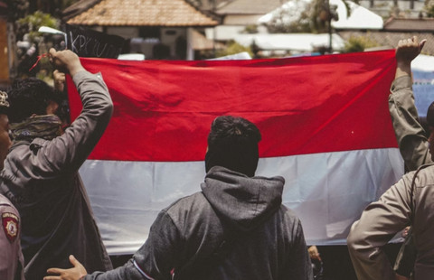 Pria dengan jaket kulit hitam memegang bendera. sumber: unsplash 