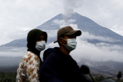 Pengendara sepeda motor melintas dengan latar belakang erupsi Gunung Semeru di Lumajang, Jawa Timur, Kamis (20/11/2025). Foto: Dipta Wahyu/REUTERS
