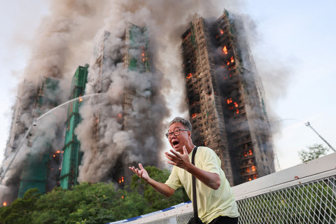 Seorang pria bereaksi saat asap mengepul sementara api melahap perancah bambu di beberapa gedung di perumahan Wang Fuk Court, Tai Po, Hong Kong, Rabu (26/11/2025). Foto: Tyrone Siu/REUTERS