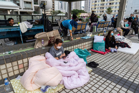 Warga beristirahat di dekat lokasi kebakaran yang terjadi pada hari Rabu di Wang Fuk Court, sebuah kompleks perumahan di distrik Tai Po, Wilayah Baru Hong Kong, Kamis (27/11/2025). Foto: Chan Long Hei/AP Photo