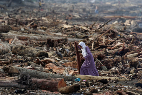 Seorang perempuan berjalan di antara batang-batang pohon yang terdampar di pantai setelah banjir bandang dan tanah longsor yang mematikan, di Padang, Provinsi Sumatera Barat, Minggu (30/11/2025). Foto: Willy Kurniawan/REUTERS