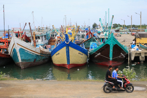 Warga mengendarai sepeda motor saat melintas di depan kapal nelayan menjelang libur melaut pada peringatan 21 tahun bencana Tsunami Aceh, 26 Desember 2025 di Pelabuhan Perikanan Lampulo, Banda Aceh, Aceh, Kamis (25/12/2025).  Foto: Ampelsa/ANTARA FOTO