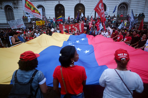 Orang-orang mengibarkan bendera Venezuela raksasa saat mereka berpartisipasi dalam demonstrasi mendukung Presiden Venezuela Nicolas Maduro di alun-alun Cinelandia di Rio de Janeiro, Brasil, Senin (5/1/2026). Foto: Mauro Pimentel/AFP