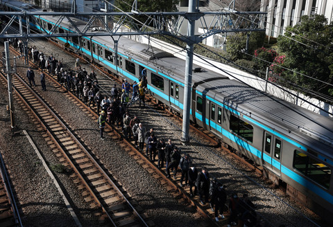Penumpang yang dievakuasi dari kereta yang terhenti di jalur Keihin-Tohoku berdiri di atas rel kereta api saat mereka menuju stasiun Tamachi di Tokyo, Jepang, Jumat (16/1/2026). Foto: Kim Kyung-Hoon/REUTERS