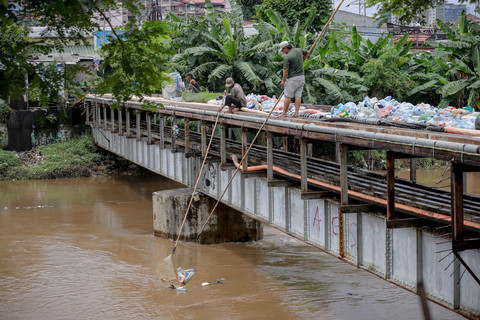 Warga menyerok botol plastik yang hanyut di aliran Sungai Ciliwung, kawasan Kebon Melati, Tanah Abang, Jakarta Pusat, Kamis (29/1/2026). Foto: Jamal Ramadhan/kumparan