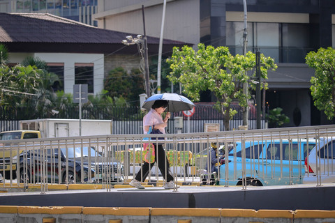 Warga menggunakan payung saat berjalan di trotoar kawasan Jalan Jenderal Sudirman, Jakarta, Senin (16/3/2026). Foto: Jamal Ramadhan/kumparan