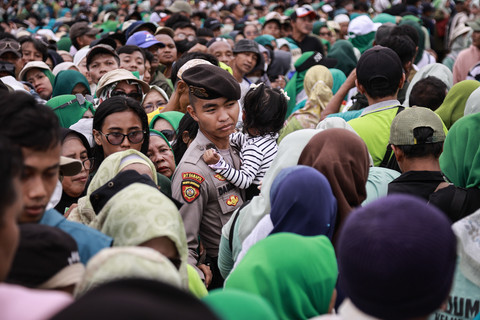 Personel kepolisian menggendong seorang anak saat orang tuanya antre menukar sembako pada Pasar Murah untuk Rakyat di kawasan Monas, Jakarta, Sabtu (28/3/2026). Foto: Dhemas Reviyanto/ANTARA FOTO