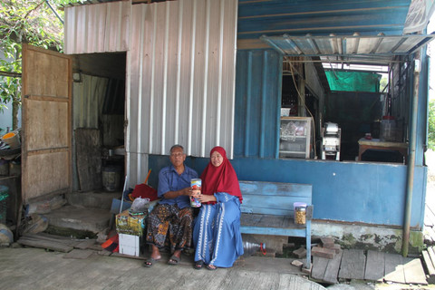 Pasangan suami istri pedagang gorengan di Kabupaten Kudus, Jawa Tengah menunjukkan kaleng tabungan di depan warungnya. Foto: Vega Maarijil Ula/kumparan