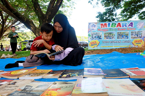 Seorang anak bersama orang tuanya membaca buku pada kegiatan Minggu Baca Ramai Ramai (MIBARA) yang digelar Pustaka Ruman Aceh di ruang terbuka hijau Blang Padang, Banda Aceh, Aceh, Minggu (19/4/2026). Foto: Akramul Muslim/ANTARA FOTO