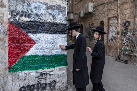 Anggota Neturei Karta, sebuah organisasi internasional Yahudi Ortodoks anti-Zionis, berdiri di samping mural yang menggambarkan bendera Palestina selama protes terhadap Negara Israel. Foto: Ilia Yefimovich/ AFP