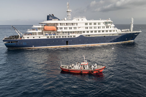 Sebuah kapal ambulans berisi kru berpakaian hazmat mendekati pintu pandu di sisi kanan kapal pesiar MV Hondius yang sedang bersandar di lepas pantai Praia, Tanjung Verde (5/5/2026). Foto: STR / AFP