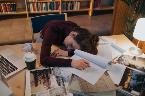 Seorang mahasiswa tertidur di meja belajar yang penuh tumpukan tugas. Bukan malas tetapi lelah dari sistem yang terus menuntut tanpa memberi makna. (Foto: Pexels/Ron Lach)