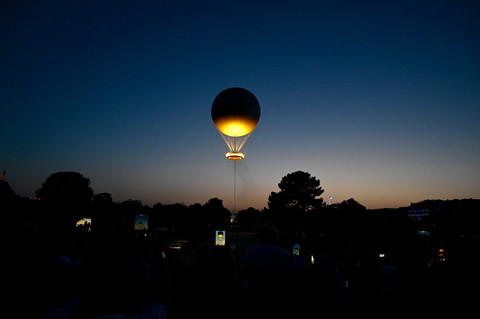 Sejumlah pengunjung merekam pemasangan kembali kaldron Olimpiade 2024 yang diikatkan ke balon, melayang di atas taman Tuileries di Paris, Prancis, Selasa (23/6/2026). Foto: Christophe DELATTRE / AFP