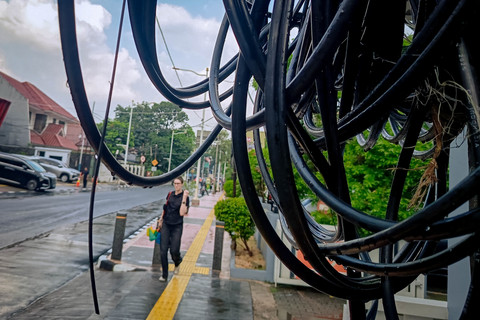 Seorang warga melintasi kabel utilitas jalur udara di kawasan Jakarta Selatan, Kamis (25/6/2026). Foto: Jamal Ramadhan/kumparan