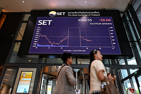 Orang-orang berjalan melewati papan elektronik yang menunjukkan pergerakan indeks saham di kantor Bursa Efek Thailand (SET) di Bangkok, Selasa (8/4/2025). Foto: Manan Vatsyayana/AFP