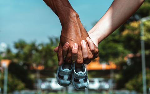 Foto kedua tangan dari dua orang yang bebeda saling berpegangan memegang sepasang sepatu anak, sumber: Pexels.com