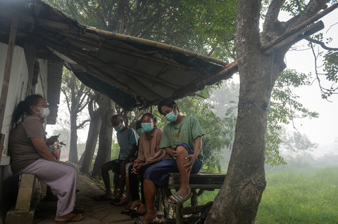 Warga terdampak asap kebakaran Tempat Pembuangan Akhir (TPA) Jatiwaringin memakai masker saat duduk di depan rumahnya di Rajeg, Kabupaten Tangerang, Banten, Jumat (3/7/2026).  Foto: ANTARA FOTO/Putra M. Akbar