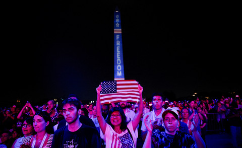 Seorang wanita mengibarkan bendera AS pada pawai Hari Kemerdekaan 4 Juli yang menampilkan Presiden AS Donald Trump, menandai peringatan 250 tahun kemerdekaan AS, di National Mall di Washington, D.C., AS, Sabtu (4/7/2026). Foto: Evan Vucci/REUTERS