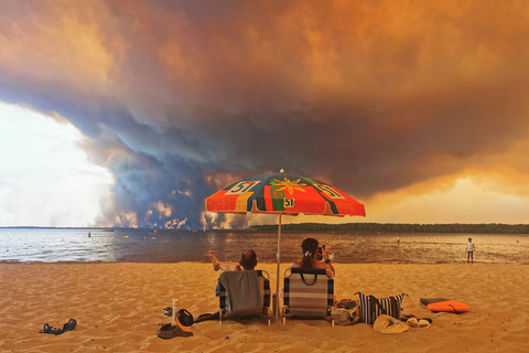Wisatawan bersantai di pantai Lacanau saat kepulan asap membubung ke langit akibat kebakaran hutan di utara cekungan Arcachon, Prancis barat daya, Jumat (24/7/2026). Foto: Maximilien LAMY / AFP