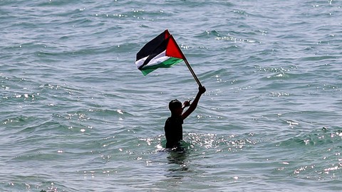 Seorang warga Palestina mengibarkan bendera negaranya selama protes menandai 'Land Day' di pelabuhan Kota Gaza, Palestina pada Rabu (30/3/2022).
 Foto: Suhaib Salem/REUTERS