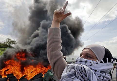 Seorang wanita Palestina menutupi wajahnya dengan kefiyeh di depan ban yang terbakar selama protes terhadap pemukiman di wilayah pendudukan pada kesempatan Hari Perempuan Internasional di desa Burqa, Tepi Barat, Nablus pada Senin (7/3/2022)   Foto: Jaafar Ashtiyeh/AFP