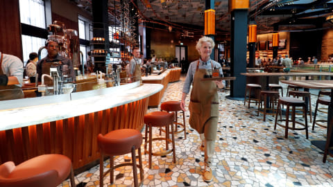 Seorang pramusaji sedang mengantarkan hidangan di gerai pertama Starbucks di Itali. Foto: REUTERS/Stefano Rellandini