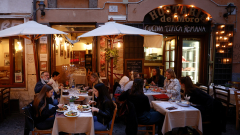 Orang-orang menikmati makanan di restoran di meja luar ruangan, di Roma, Italia, Senin (26/4). Foto: Guglielmo Mangiapane/REUTERS