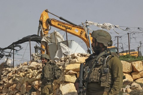 Seorang tentara Israel berjaga-jaga ketika alat berat menghancurkan rumah keluarga Palestina, di selatan kota Hebron, Tepi Barat pada Rabu (9/3/2022)
 Foto: Hazem Bader/AFP
