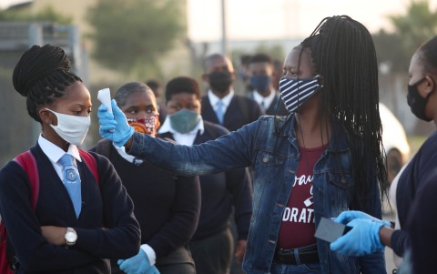 Seorang guru memeriksa suhu siswa sebelum masuk sekolah untuk pertama kali setelah lockdown akibat virus corona di Cape Town, Senin (8/6). Foto: Reuters/Mike Hutchings