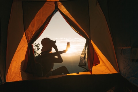 Seorang traveler perempuan memotret pemandangan gunung dari depan kemahnya  Foto: Shutterstock