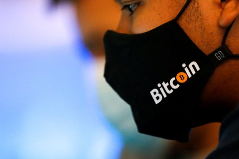 Seorang pria mengenakan masker Bitcoin duduk di sebuah kafe yang menampilkan tren dan harga terbaru berbagai cryptocurrency di Nakhon Ratchasima, Thailand. Foto: Soe Zeya Tun/REUTERS